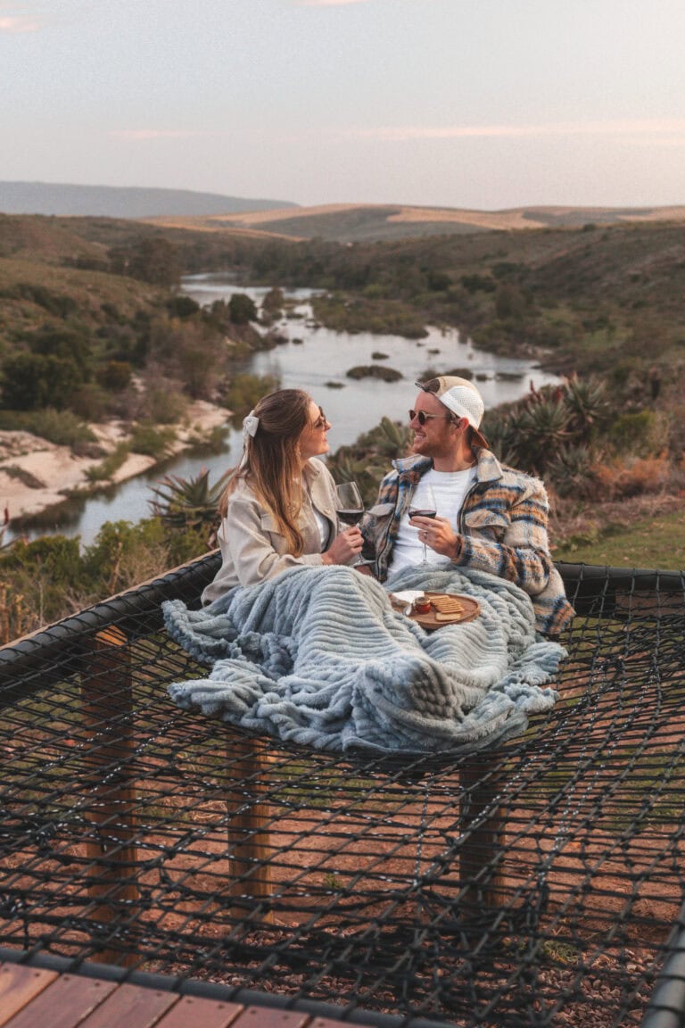 young couple having drinks on a cargo net with a scenic background stay@napky cabin